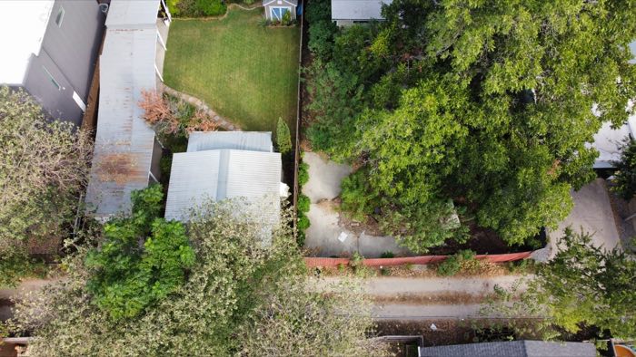 Straight-down aerial of the rear yards and outbuildings with the alley running along the bottom of the frame.