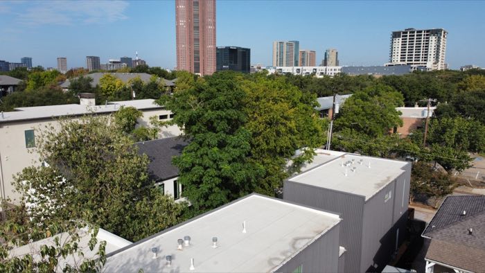 Aerial looking toward the downtown Dallas skyline over the rooftops of nearby modern townhomes.