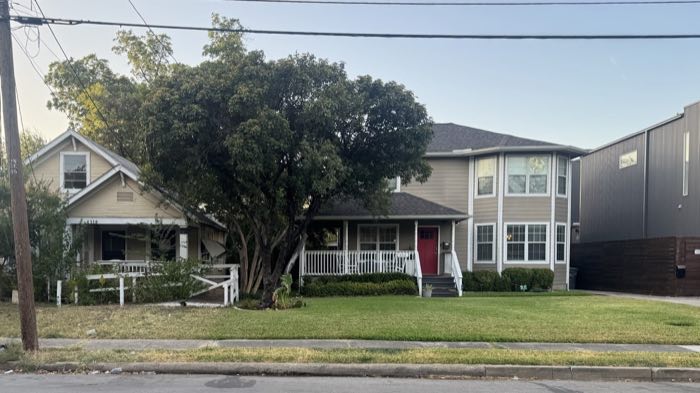 Street-level view of both Deere Street properties from across the road: a weathered single-storey craftsman at left, a renovated two-storey house at right, with open front lawns.